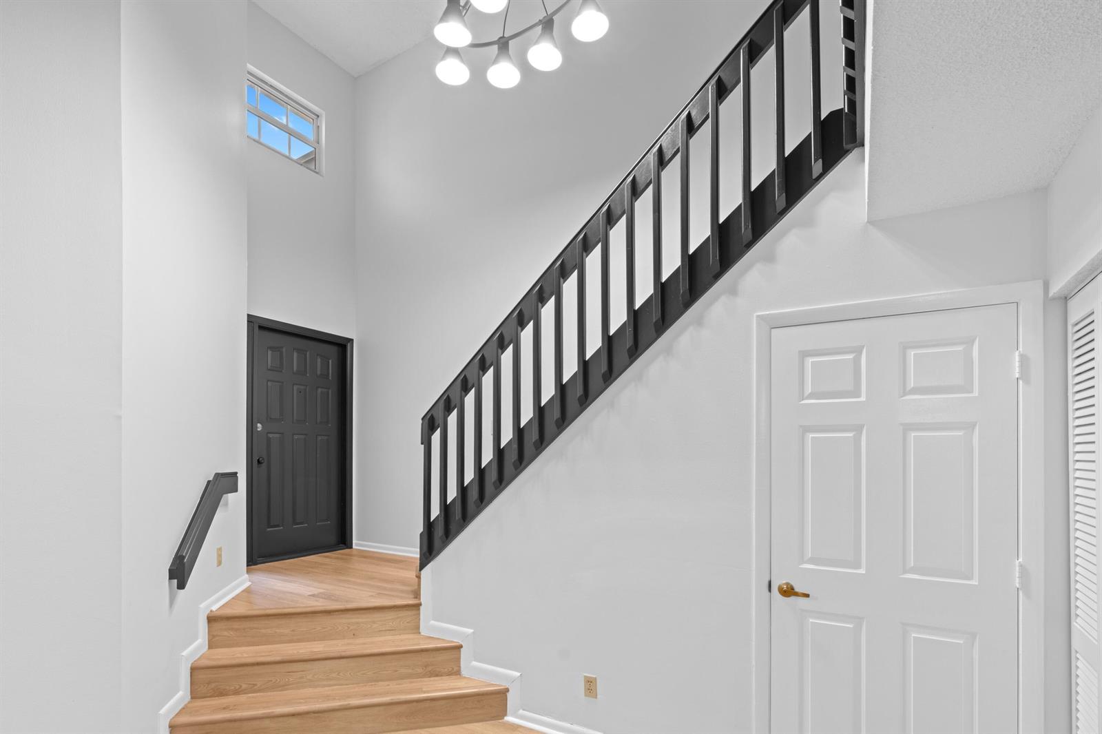 A foyer features light wood stairs, a black railing, a black door, and a modern chandelier — 1410 Ocean Dunes Circle, Jupiter FL 33477, JUPITER, FL