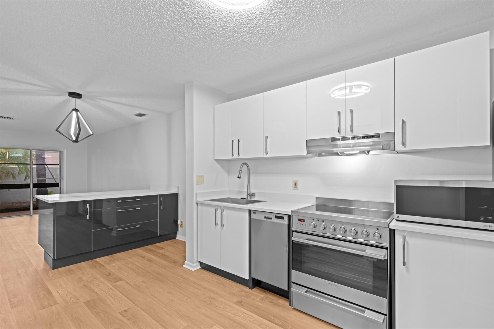 A modern kitchen features white upper cabinets, dark lower cabinets, stainless steel appliances, and wood flooring — 1410 Ocean Dunes Circle, Jupiter FL 33477, JUPITER, FL
