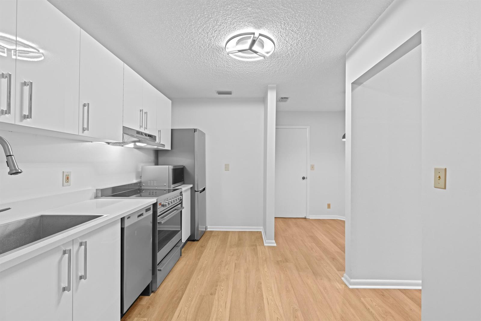 A kitchen with white cabinets, stainless steel appliances, and light wood-look flooring — 1410 Ocean Dunes Circle, Jupiter FL 33477, JUPITER, FL