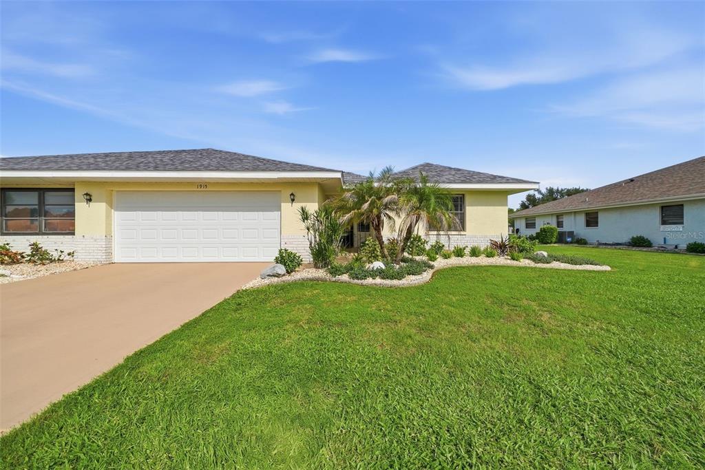 A single-story house with a yellow exterior, a two-car garage, and a landscaped front yard — 1915 W DEL WEBB BOULEVARD, SUN CITY CENTER, FL