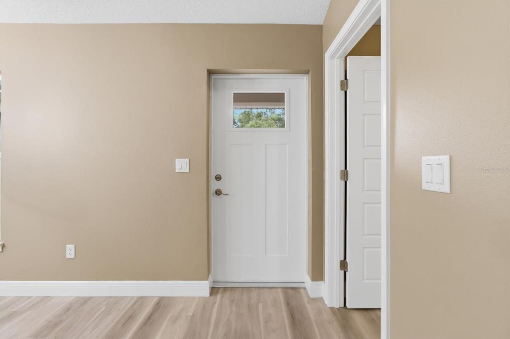 A room with tan walls, light wood-look flooring, a white exterior door, and an open doorway — 9944 N WAYLAND AVENUE, CITRUS SPRINGS, FL