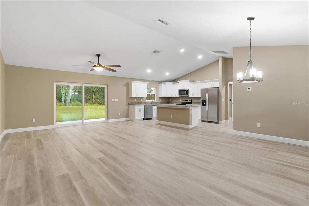 An open-concept kitchen and living area features light wood flooring, white cabinetry, and granite countertops — 9944 N WAYLAND AVENUE, CITRUS SPRINGS, FL