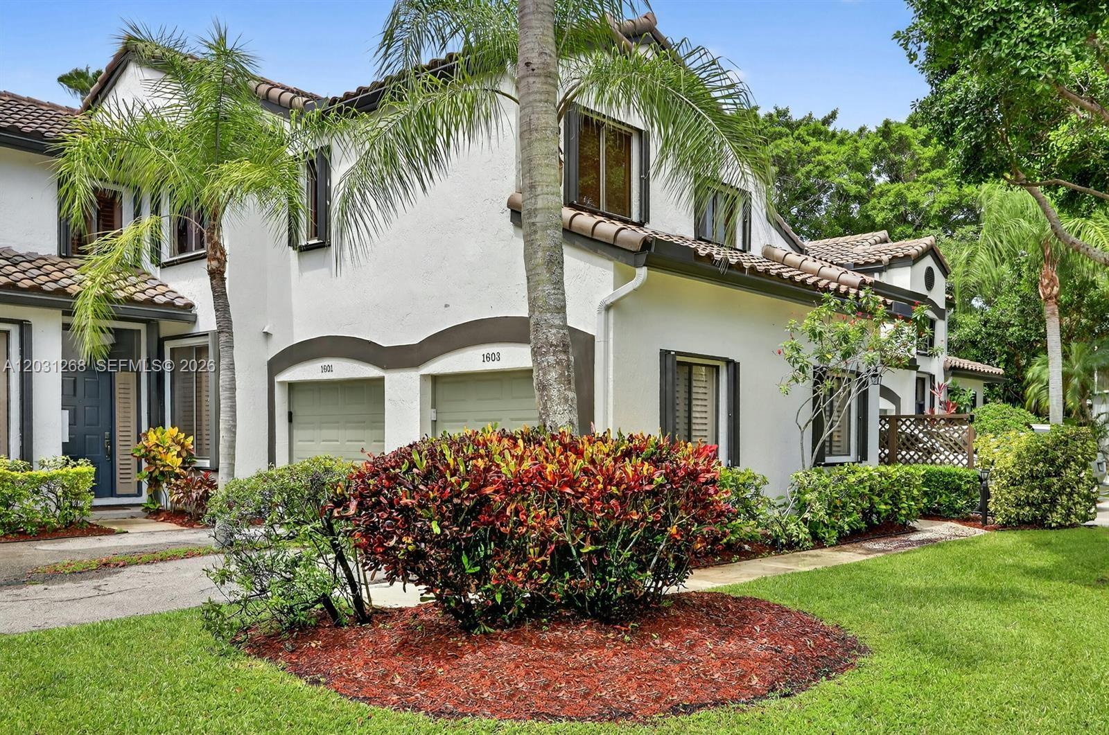 A two-story white stucco townhouse features a tile roof, two garage doors, and landscaped gardens — 7525 NW 61st Ter # 1603, Parkland FL 33067, PARKLAND, FL