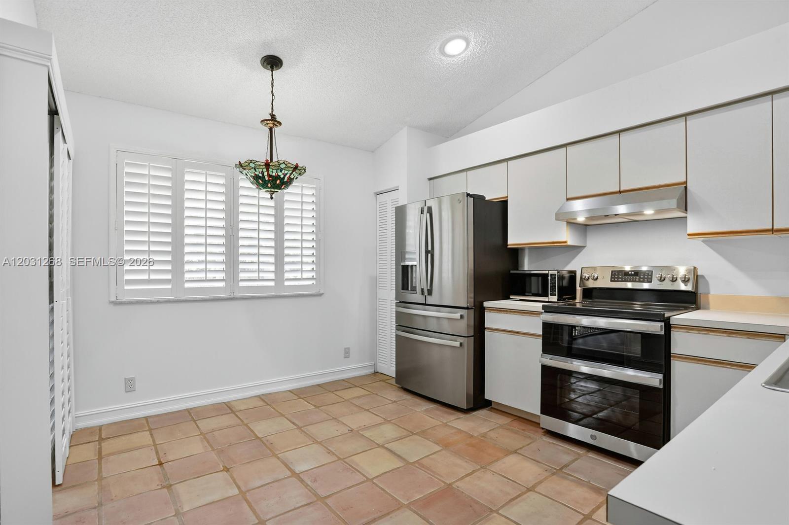 A kitchen features white cabinets, stainless steel appliances, and terracotta tile flooring — 7525 NW 61st Ter # 1603, Parkland FL 33067, PARKLAND, FL