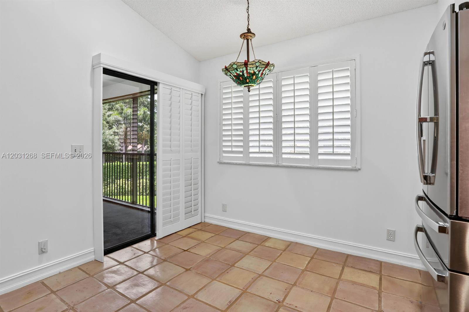 A dining area features tile flooring, a stained-glass chandelier, plantation shutters, and a sliding door — 7525 NW 61st Ter # 1603, Parkland FL 33067, PARKLAND, FL
