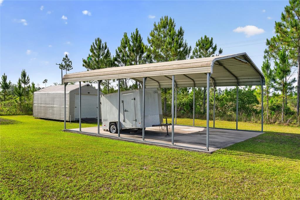 A metal carport shelters a small utility trailer next to a detached storage shed — 8433 LIMONIA DRIVE, INDIAN LAKE ESTATES, FL