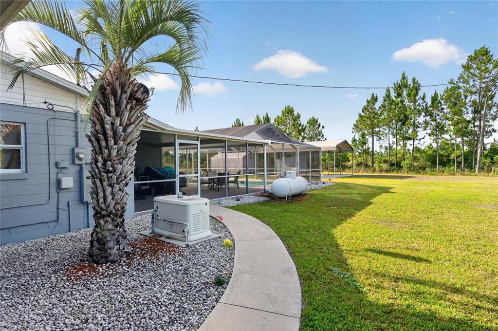 A backyard view showing a house with a screened-in pool, generator, and propane tank — 8433 LIMONIA DRIVE, INDIAN LAKE ESTATES, FL
