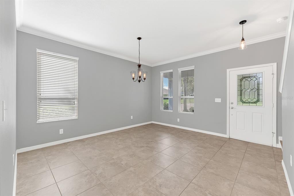 An empty dining room features gray walls, tile flooring, a chandelier, and a front door — 5101 SANDERLING RIDGE DRIVE, LITHIA, FL