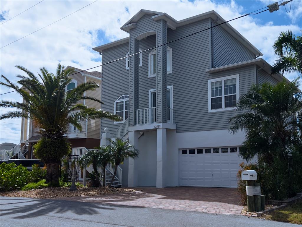 A three-story gray house with a white garage and a small balcony stands outdoors — 13737 VICTOR AVENUE, HUDSON, FL