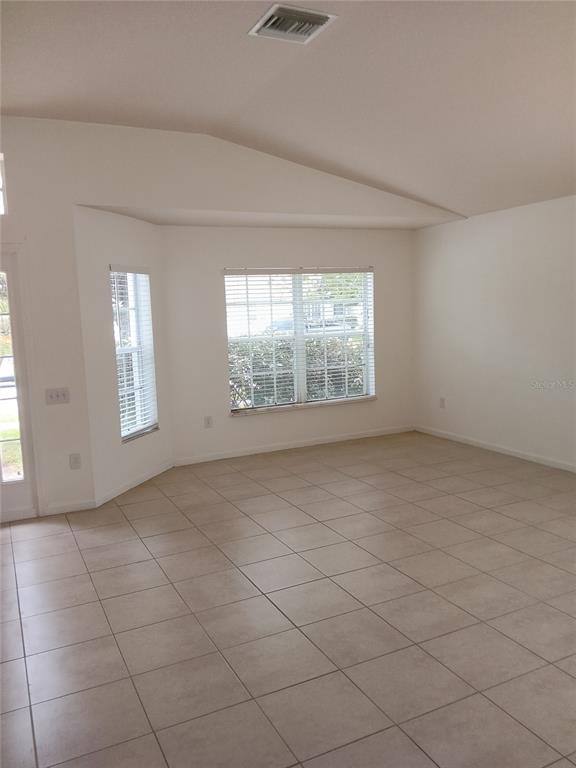 A bright, empty room features light-colored tile flooring, white walls, and a vaulted ceiling — 7733 OUTERBRIDGE STREET, WESLEY CHAPEL, FL