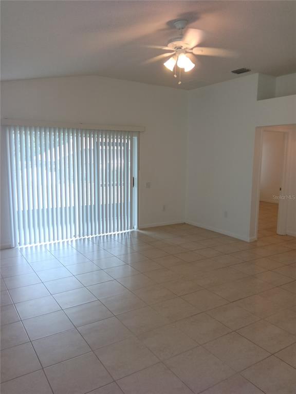 A living room with light-colored tile flooring, a ceiling fan, and sliding glass patio doors — 7733 OUTERBRIDGE STREET, WESLEY CHAPEL, FL