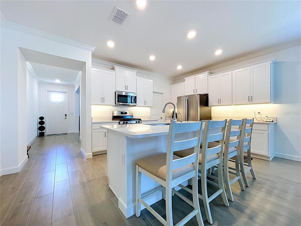 A white kitchen features a central island with bar stools and stainless steel appliances — 5524 LITTLE PATH DRIVE, WIMAUMA, FL
