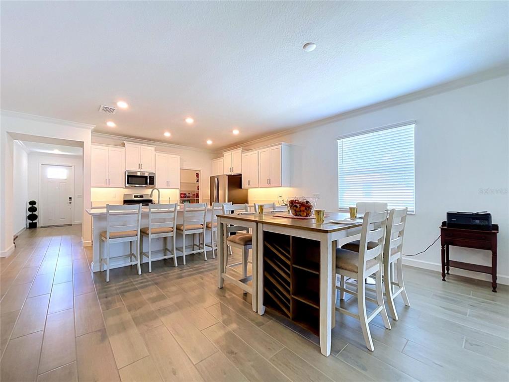 A kitchen features white cabinetry, a central island with seating, and light-colored tile flooring — 5524 LITTLE PATH DRIVE, WIMAUMA, FL