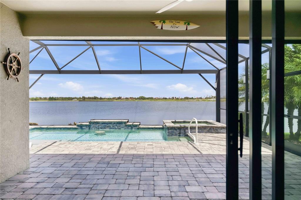 A covered patio overlooks a swimming pool, spa, and a large lake beyond the screen enclosure — 24100 SPARTINA DRIVE, VENICE, FL