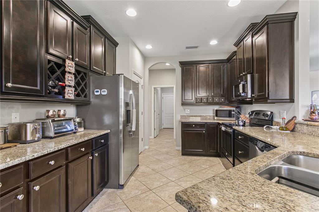 A kitchen features dark wood cabinets, granite countertops, stainless steel appliances, and tile flooring — 29255 GRASS BUNKER DRIVE, SAN ANTONIO, FL