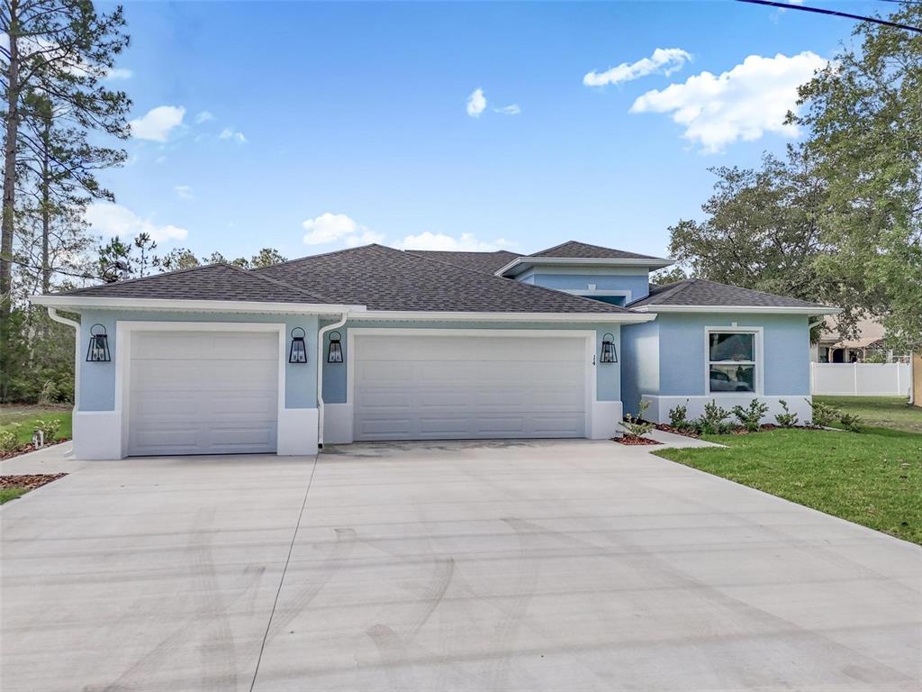 A light blue house with a three-car garage and a concrete driveway under a sky — 14 WHITE BIRCH LANE, PALM COAST, FL