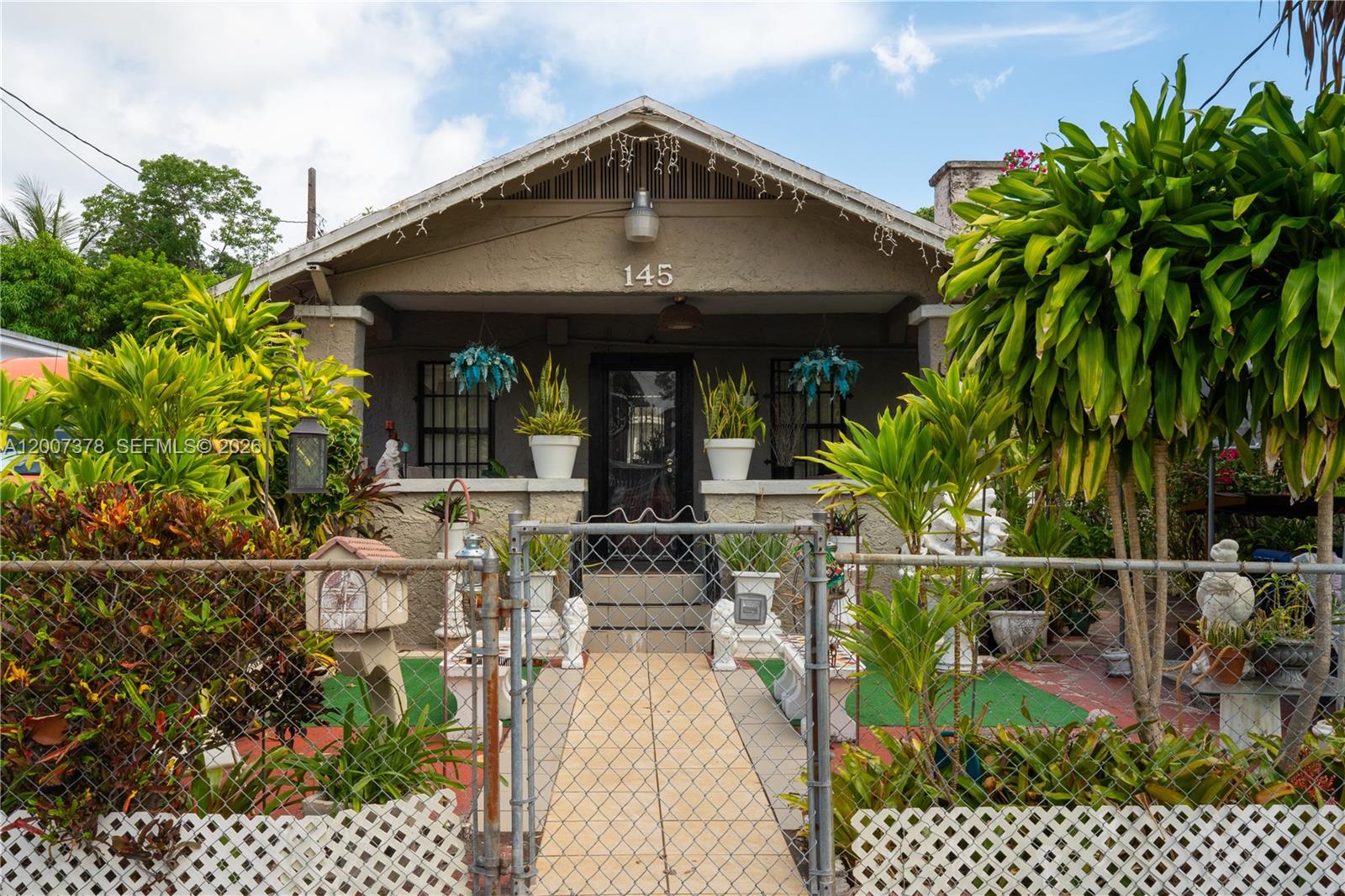 A single-story house with a front porch, chain-link fence, and lush landscaping — 145 NW 31st St, Miami FL 33127, MIAMI, FL