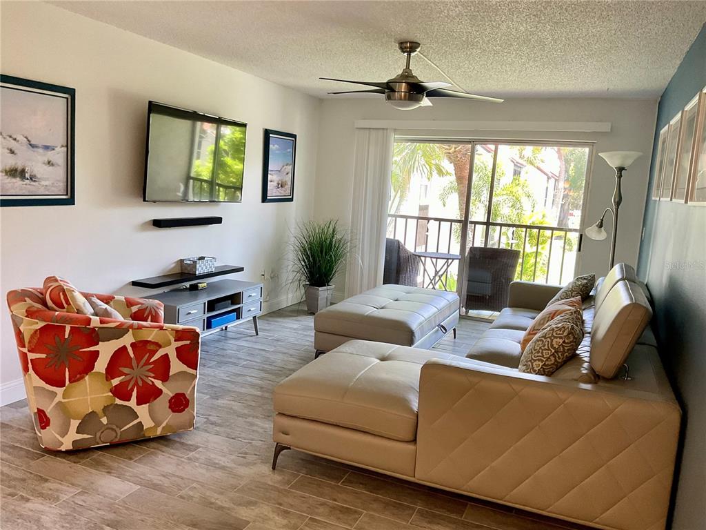 A living room features a tan sectional sofa, a floral armchair, and a sliding glass door — 3213 BENEVA ROAD UNIT 204, SARASOTA, FL