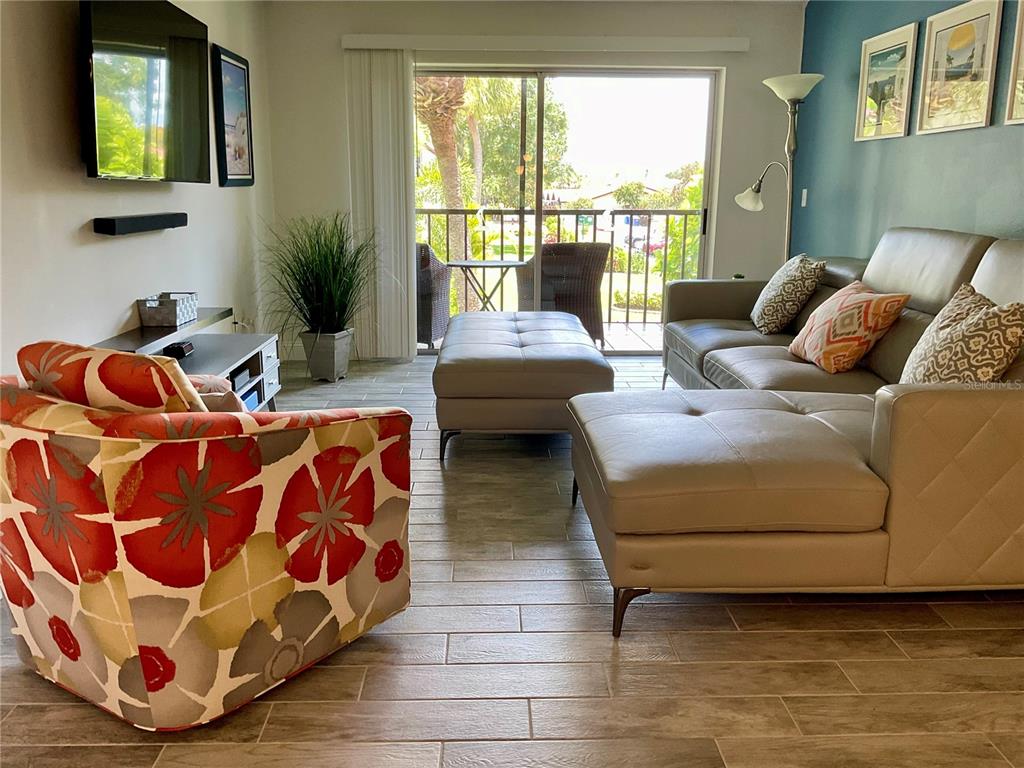 A living room features a floral armchair, a gray sectional sofa, and a balcony view — 3213 BENEVA ROAD UNIT 204, SARASOTA, FL