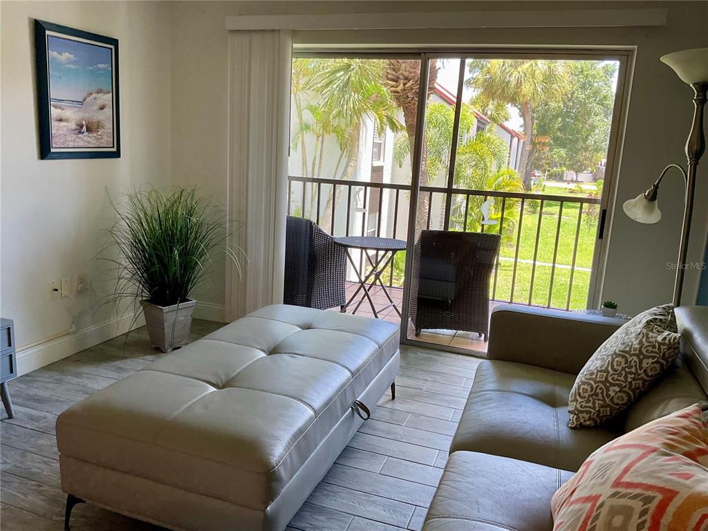 A living room features a gray ottoman, a sofa, and a balcony with outdoor seating — 3213 BENEVA ROAD UNIT 204, SARASOTA, FL