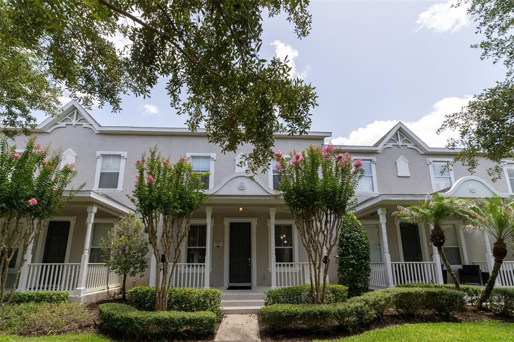 A row of townhouses with front porches, white railings, and manicured hedges under a blue sky — 3933 CLEARY WAY, ORLANDO, FL