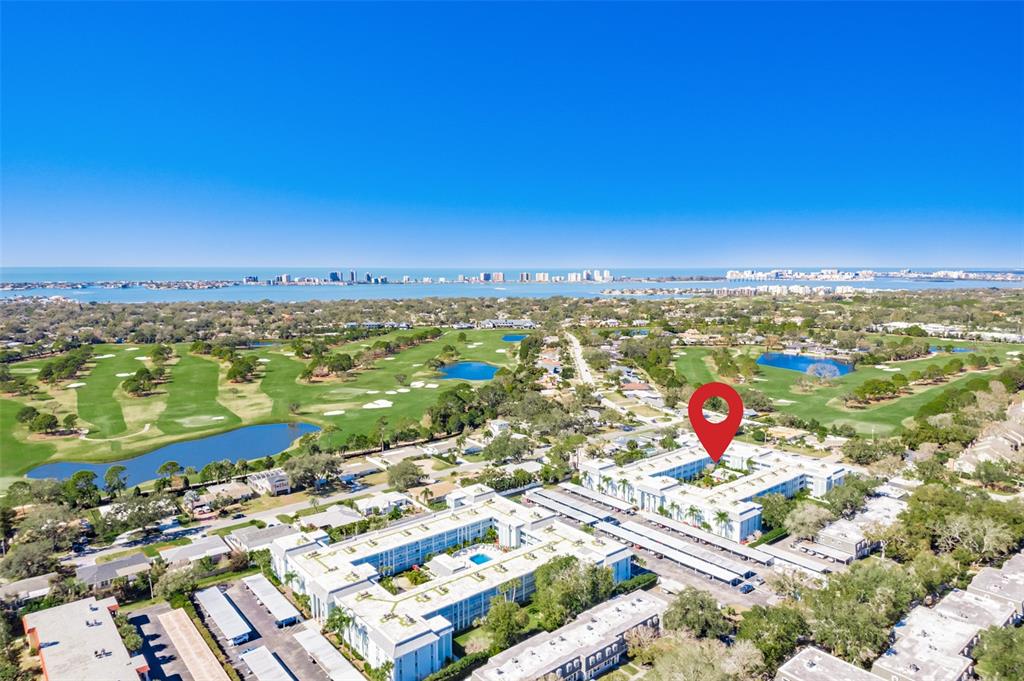 An aerial view shows a multi-story apartment complex situated next to a golf course — 701 POINSETTIA ROAD UNIT 208, BELLEAIR, FL