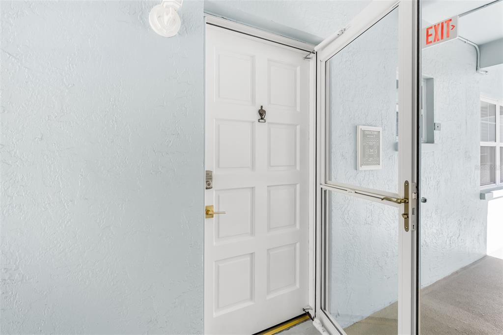 A white front door with a brass knocker is visible behind a glass storm door — 701 POINSETTIA ROAD UNIT 208, BELLEAIR, FL