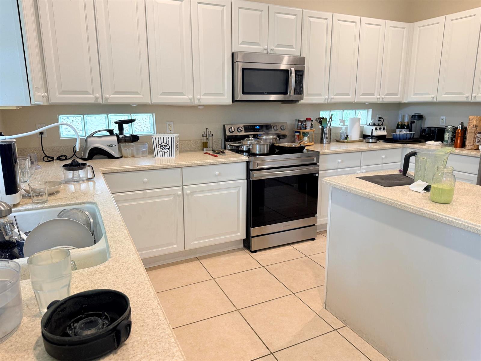 A kitchen features white cabinets, stainless steel appliances, and light-colored countertops over tile flooring — 17 Country Lake Circle, Boynton Beach FL 33436, BOYNTON BEACH, FL