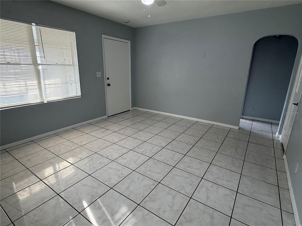 An empty room features light gray walls, white tile flooring, a window with blinds, and an arched doorway — 2705 6TH STREET W, BRADENTON, FL