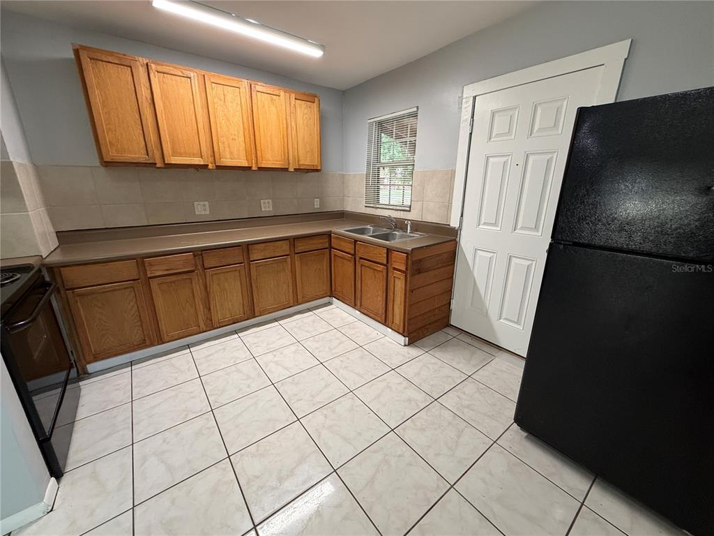 A kitchen features wood cabinets, tile flooring, a double sink, and a black refrigerator — 2705 6TH STREET W, BRADENTON, FL