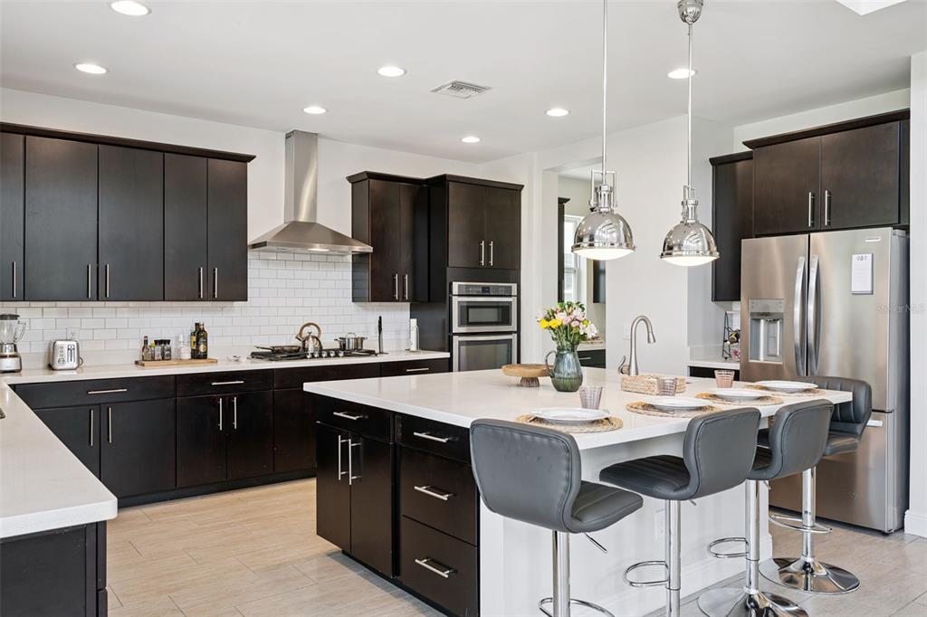 A modern kitchen features dark wood cabinets, white countertops, stainless steel appliances, and a center island — 7211 STILL POND LANE, WINDERMERE, FL