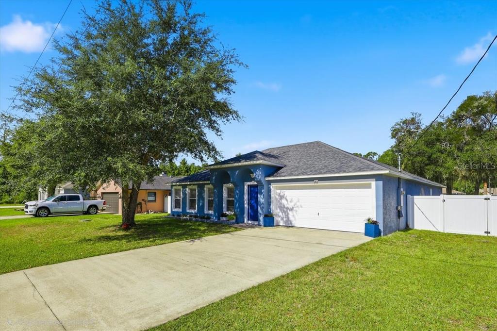 A blue, single-story house with a white garage door and a large tree in front — 41 ZEPHYR LILY TRAIL, PALM COAST, FL