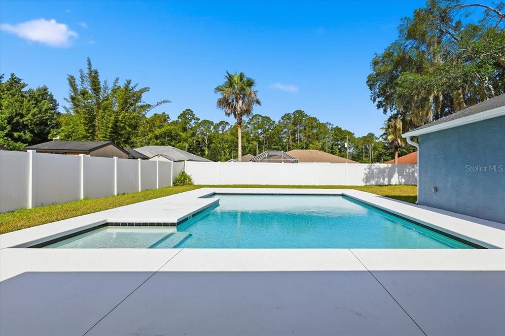 A backyard features a rectangular swimming pool with a shallow tanning ledge and white fencing — 41 ZEPHYR LILY TRAIL, PALM COAST, FL