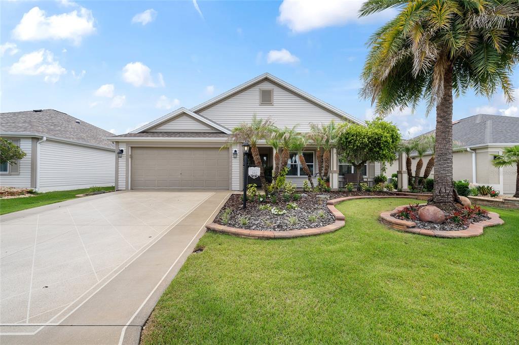A single-story house with a beige garage, a palm tree, and a landscaped front yard — 387 HARLOW LANE, THE VILLAGES, FL