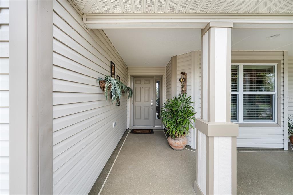 A covered front porch features light-colored vinyl siding, a gray door, and a potted plant — 387 HARLOW LANE, THE VILLAGES, FL