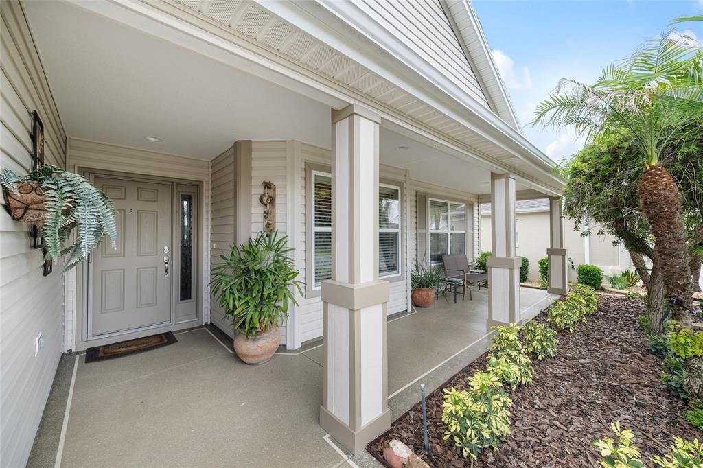 A covered front porch with beige siding, square columns, and a gray front door — 387 HARLOW LANE, THE VILLAGES, FL