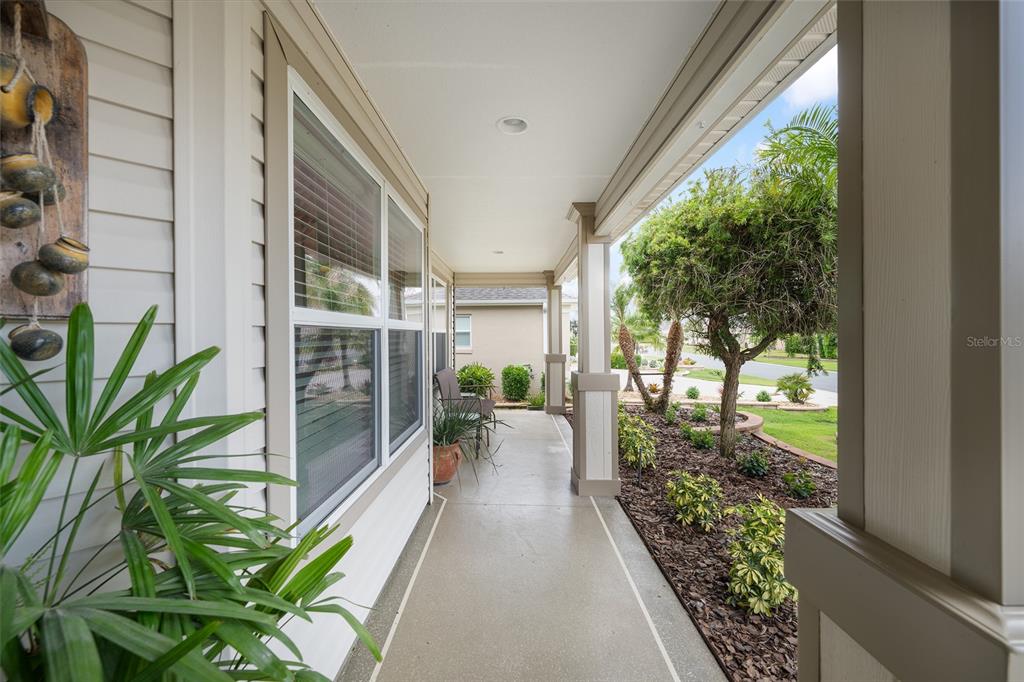 A covered front porch features a concrete floor, light-colored siding, and a landscaped garden bed — 387 HARLOW LANE, THE VILLAGES, FL