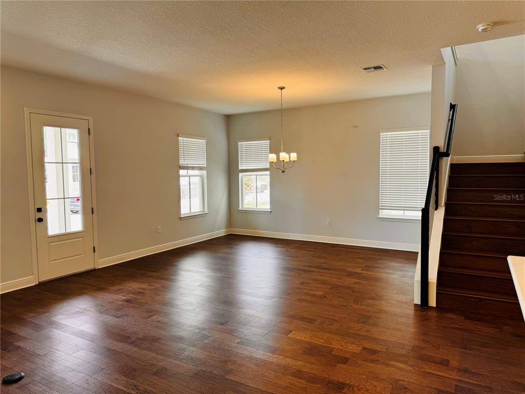 An empty room with hardwood floors, a chandelier, and a staircase leading to the upper level — 10120 PEEBLES STREET, ORLANDO, FL