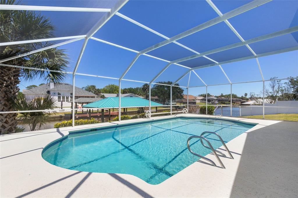 A swimming pool with a screened enclosure overlooks a canal and a boat dock — 21 CRESCENT COURT S, PALM COAST, FL