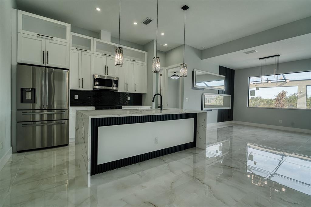 A modern kitchen features white cabinetry, a marble-topped island, and glossy tile flooring — 10474 WINNIPEG STREET, PORT CHARLOTTE, FL
