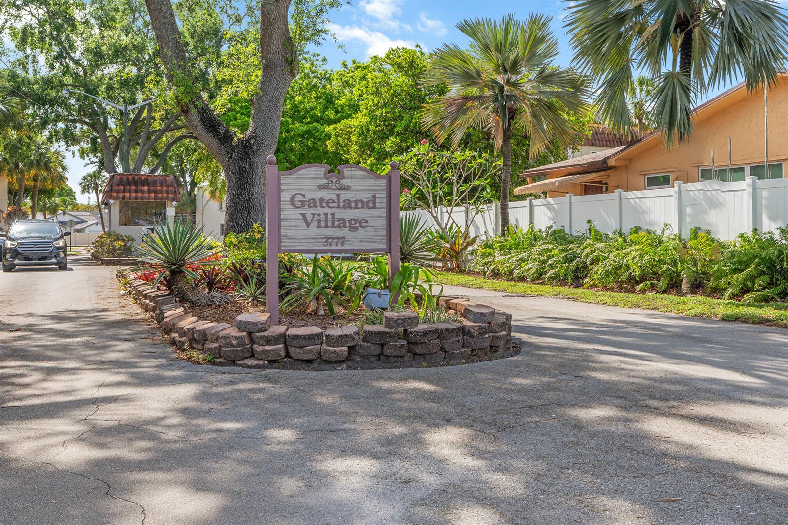 A sign for Gateland Village stands in a landscaped island at the entrance of a community — 3777 NW 78th Avenue # 1b, Davie FL 33024, DAVIE, FL