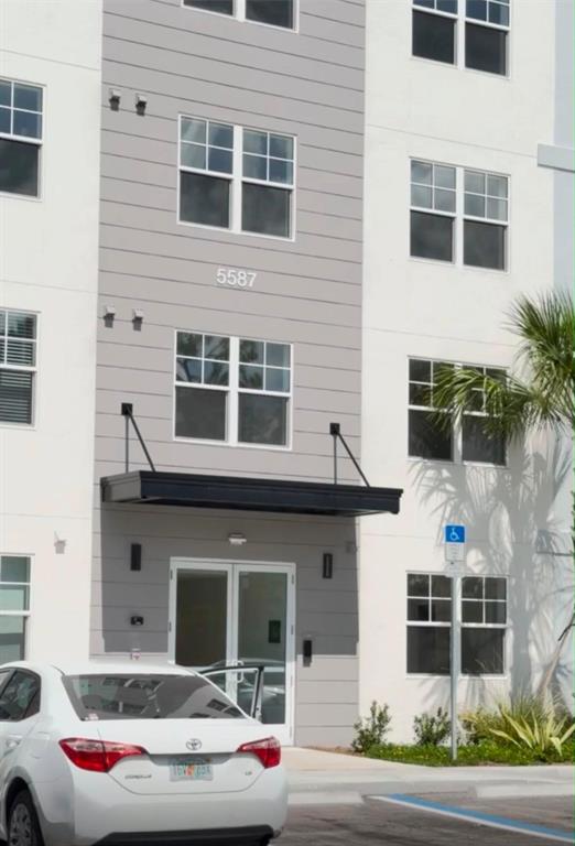 A white and gray multi-story apartment building exterior with a black metal entrance awning — 5587 MILLENIA PARK BLVD UNIT 418, ORLANDO, FL