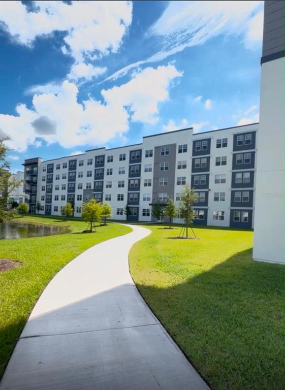 A multi-story apartment building exterior features a curved concrete walkway and a small pond — 5587 MILLENIA PARK BLVD UNIT 418, ORLANDO, FL