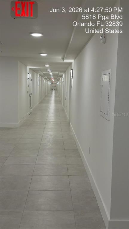 A long, brightly lit indoor hallway with white walls and light gray tiled flooring — 5587 MILLENIA PARK BLVD UNIT 418, ORLANDO, FL