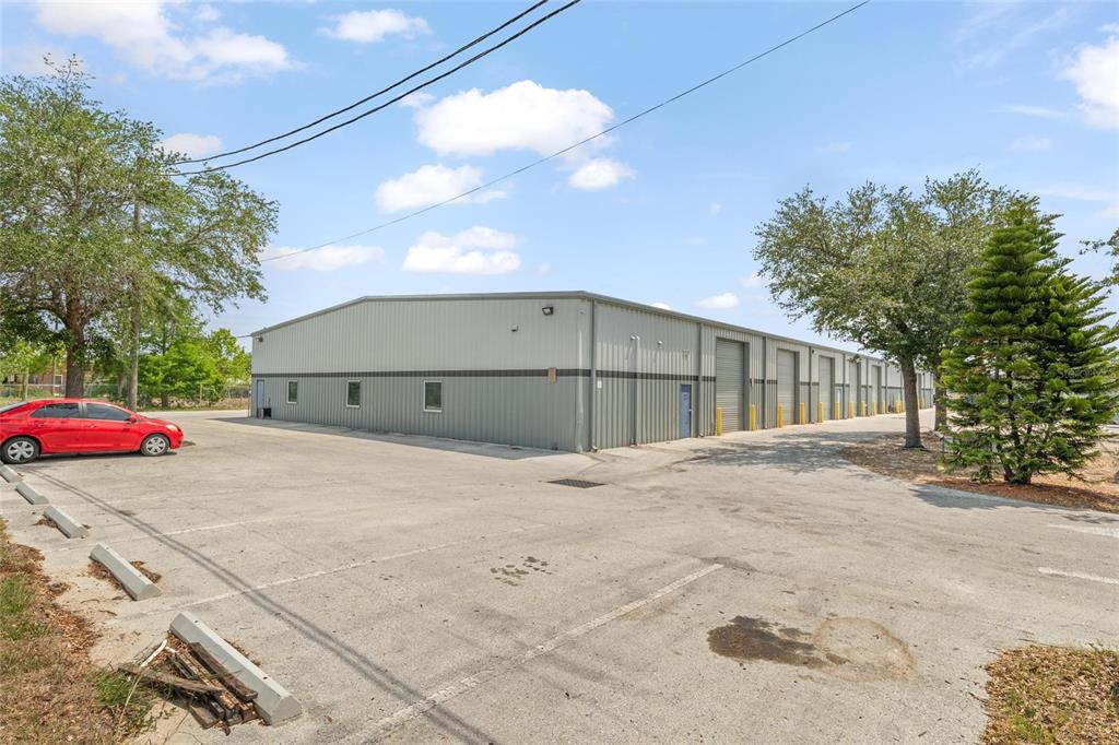 A single-story metal warehouse building features multiple roll-up doors and an adjacent paved parking lot — 1500 L AND R INDUSTRIAL BOULEVARD Bldg. D, TARPON SPRINGS, FL