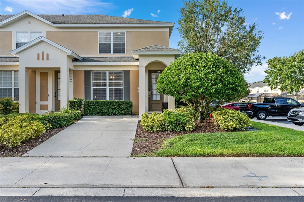A two-story townhouse exterior features a concrete driveway, manicured landscaping, and a dark pickup truck — 7667 OTTERSPOOL STREET, KISSIMMEE, FL