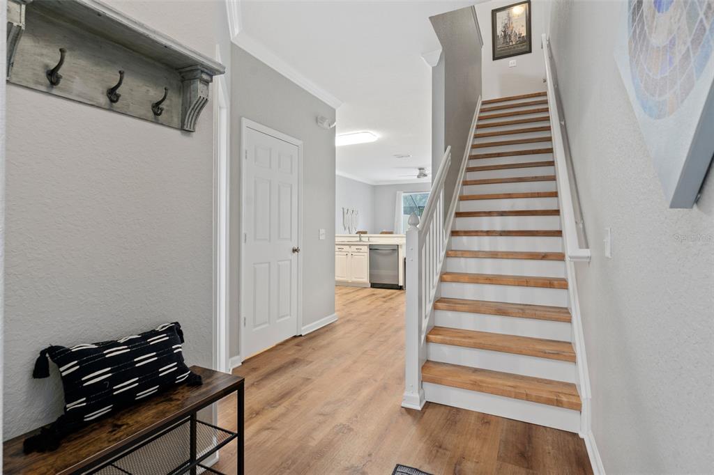 An entryway features a wooden staircase, a coat rack, a bench, and a view into a kitchen — 7667 OTTERSPOOL STREET, KISSIMMEE, FL