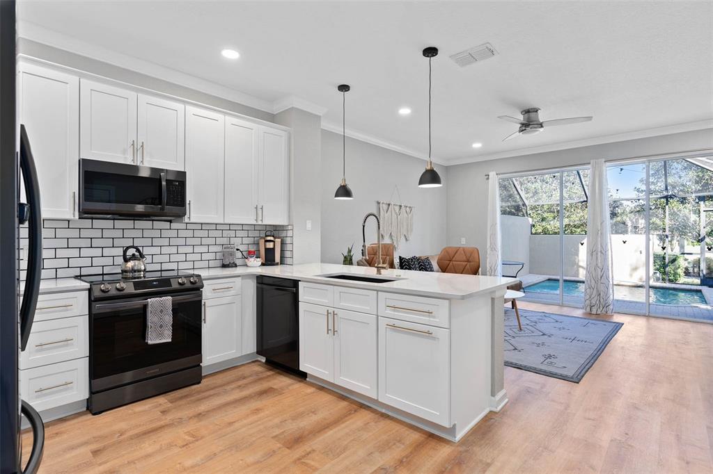A kitchen with white cabinets, black appliances, and an island overlooking a pool and patio — 7667 OTTERSPOOL STREET, KISSIMMEE, FL