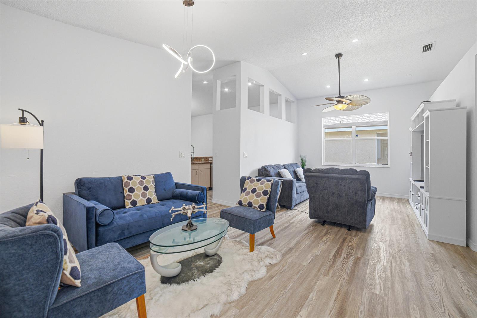 A living room features blue sofas, a glass coffee table, and light wood-look flooring — 8057 Stirrup Cay Court, Boynton Beach FL 33436, BOYNTON BEACH, FL