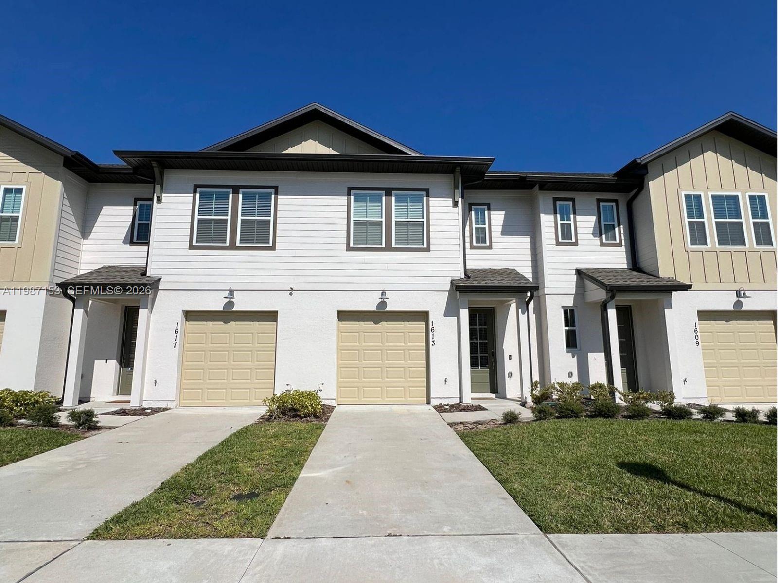 A row of three modern townhouses with beige garage doors and white siding under a clear sky — 1613 PELICAN DRIVE, Davenport FL 33896, DAVENPORT, FL